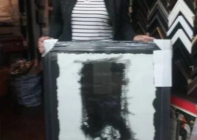 A woman holding a framed painting in a store.